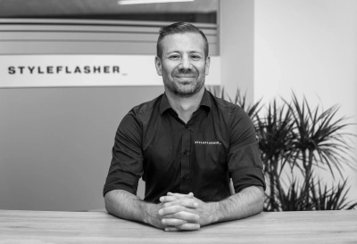 Andreas Adelsberger, Geschäftsführung von Styleflasher, sitzt am Tisch mit gefalteten Händen vor Firmenlogo im Büro